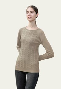 Sweater en tricot beige avec des manches longues et un col rond, arborant un motif texturé et une silhouette ajustée. Porté avec un jean foncé.