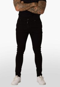 Jeans negros ajustados de mezclilla, con bolsillos delanteros, cierre de cremallera y corte slim. Combinados con zapatillas blancas.