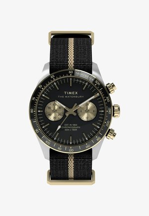 Timex Waterbury óra fekete számlappal, arany díszítésekkel, kronográf funkciókkal és egy fekete szövetpánttal, amelyen függőleges arany csík található.