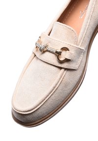 Mocassino in suede beige con punta arrotondata, caratterizzato da una fascetta in oro con strass e una suola in gomma piatta. Texture liscia su tutta la superficie.