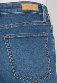Dark blue denim jeans with a subtle texture. Features a back pocket and a tan leather label at the waistband with "SOCX DENIM" embossed.