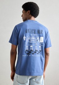 Blauwe katoenen T-shirt met een graphic op de rug met de tekst "ANTICO BAR", barillustraties en krukken. Lichtgewicht stof, casual pasvorm.