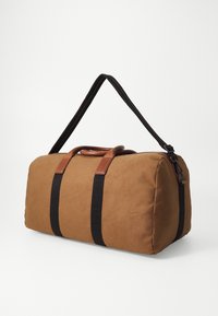 Borsa da viaggio in tessuto marrone con cinghie in rete nere, dettagli in pelle marrone a contrasto, forma arrotondata, texture liscia e chiusura con zip.