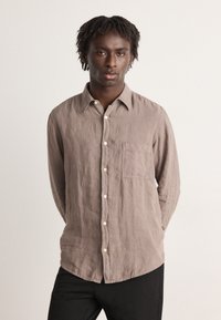 Camicia di lino marrone chiaro con chiusura a bottoni, taschino sul petto e colletto a punta. Tessuto texturizzato e vestibilità rilassata.