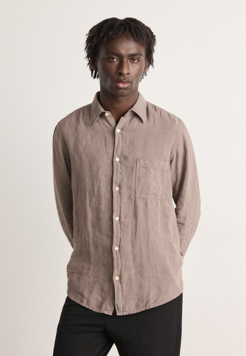 Camicia di lino marrone chiaro con chiusura a bottoni, taschino sul petto e colletto a punta. Tessuto texturizzato e vestibilità rilassata.