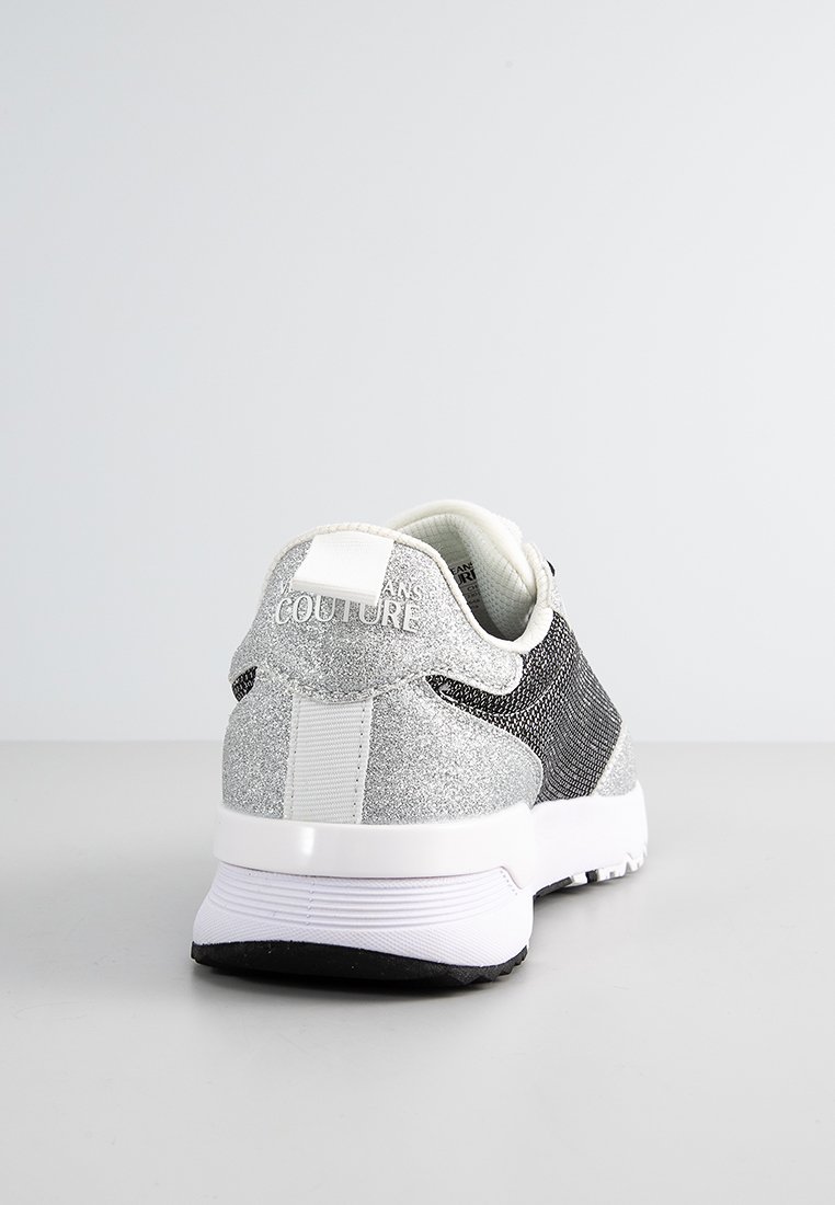 Zapatilla plateada y negra con parte superior texturizada, adornos de brillo, talón blanco liso y suela de goma. Marca en el talón.