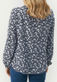 Blusa a maniche lunghe con motivo geometrico in tonalità di blu, grigio e nero. Il tessuto è leggero e presenta una texture leggermente lucida.
