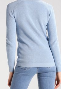 Ljusblå ribbad stickad tröja med långa ärmar och en figurnära silhuett. Har en rundad halsringning och en rak fåll.