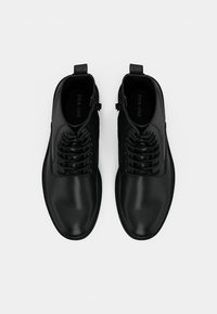 Scarpe in pelle nera con una texture liscia, punta arrotondata e un design di allacciatura intricata. Presentano un strap per il tallone per una facile vestibilità.