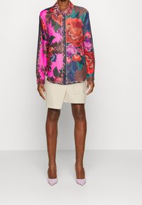 Camisa de botones colorida con un patrón floral en rosa, rojo y verde, con mangas largas, cuello y un tejido ligero.