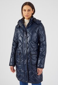 Cappotto imbottito trapuntato blu navy con colletto alto, chiusura frontale con zip, chiusura a scatto e due tasche anteriori. Presenta dettagli neri a contrasto e una texture lucida.
