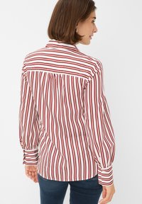 Red and white striped blouse with long sleeves, buttoned cuffs, and a pleated back detail, made from a smooth fabric.
