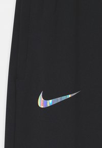 Schwarzer Stoff mit einem reflektierenden, schillernden Nike-Swoosh-Logo in der Nähe einer Naht oder Kante.
