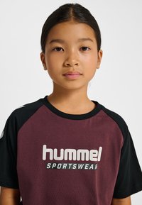 Vinröd och svart sport t-shirt med korta ärmar och "hummel"-logotyp i vitt. Rund halsringning, raglanärmar, slät tygstruktur.