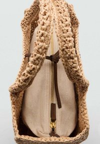 Kudottu beige reppu, jossa on tekstuurinen olkipinta, varustettuna kahdella punotulla hihnalla ja vetoketjullisella kankaisella osastolla, jossa on ruskea nahka-aksentti.