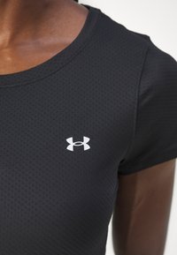 T-shirt de sport noir en tissu texturé. Présente un col rond et un petit logo blanc sur la poitrine.