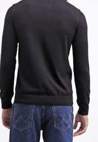 Czarny sweter o dopasowanym kroju, z prążkowanymi ściągaczami przy mankietach i dole. Nosi się go z niebieskimi dżinsami wyróżniającymi się charakterystycznym przeszyciem na tylnych kieszeniach.