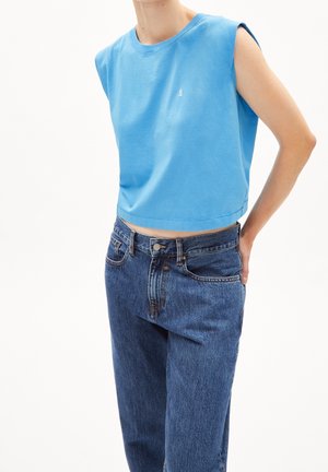 Sininen lyhythihainen puuvillapaita, jossa on pyöreä kaula-aukko ja pieni brodeerattu logo, yhdistettynä korkeavyötäröisiin farkkuihin.