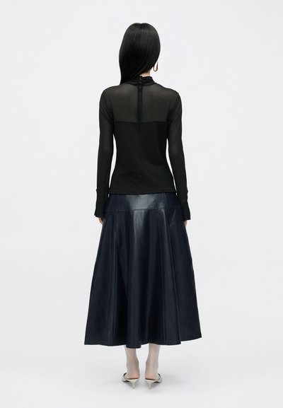 Fekete, áttetsző, hosszú ujjú felső magas nyakkal, sötétkék bőr A-vonalú szoknyával párosítva, melynek hátul cipzárja és bővülő szegélye van.