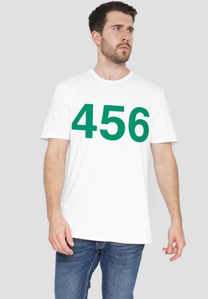 White cotton t-shirt featuring large green numbers "456" on the front. Short sleeves and crew neck design. Worn with blue jeans.