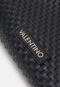 Black woven leather clutch bag featuring a rectangular shape, a visible logo patch with gold lettering, and a textured surface.