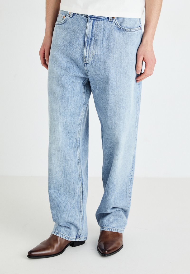 Jean en denim bleu clair avec une coupe droite, cinq poches et une taille classique, associés à des bottes en cuir marron foncé à bout pointu.