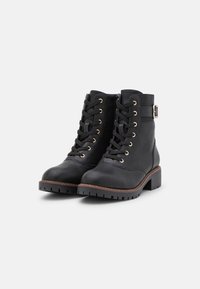 Botines negros de cuero con suela gruesa, ojales dorados y hebilla decorativa. Presentan una punta redondeada y un cierre de cordones en la parte frontal.