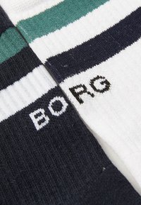 Zwei Paar Stricksocken mit horizontalen Streifen; eines in Marineblau und Weiß, das andere in Grün, Weiß und Marineblau, beide mit teilweise sichtbar "BO" und "PG" Text.