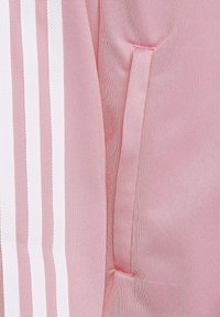 Rosa Sportjacke mit weißen Streifen, glatter Textur und einer Reißverschlusstasche an der Seite für sichere Aufbewahrung.