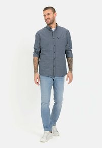 Overhemd met knopen in een marineblauw en wit geruite stof, van katoen, met lange mouwen die opgerold zijn, gecombineerd met lichtblauwe jeans en witte sneakers.