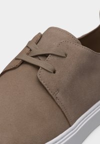 Ανοιχτό καφέ καστόρινο παπούτσι casual με κορδόνια στο ίδιο χρώμα και λευκή καουτσούκ σόλα, εμφανίζεται σε κοντινή λήψη σε λευκό φόντο.