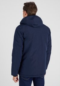 Giacca blu navy con cappuccio, dal tessuto liscio, con un taglio dritto, polsini elasticizzati e un dettaglio di cucitura sulla schiena. Vestibilità casual.