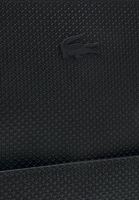 Black textured bag with a patterned surface and a prominent black crocodile logo. Features a structured design and smooth edges.