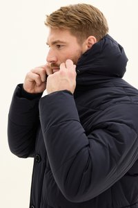 Granatowa kurtka puchowa z wysokim kołnierzem, z pikowaną fakturą, zapięciem na guziki oraz regulowanym kapturem. Materiał wydaje się gładki i ocieplany.