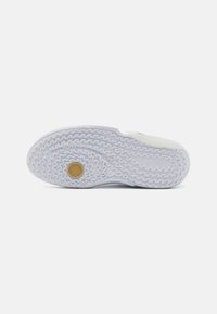 Semelle de sneaker blanche avec un motif en zigzag texturé, présentant un logo circulaire doré au centre. Fini en matériau lisse, bords arrondis.