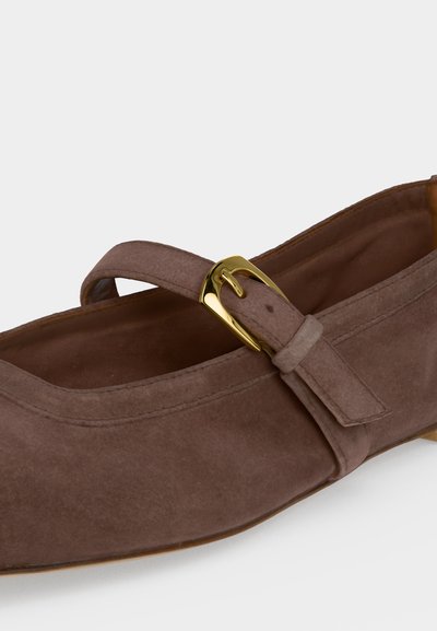 Chaussure Mary Jane en daim marron avec une boucle dorée et une bride sur le dessus, sur fond blanc uni.