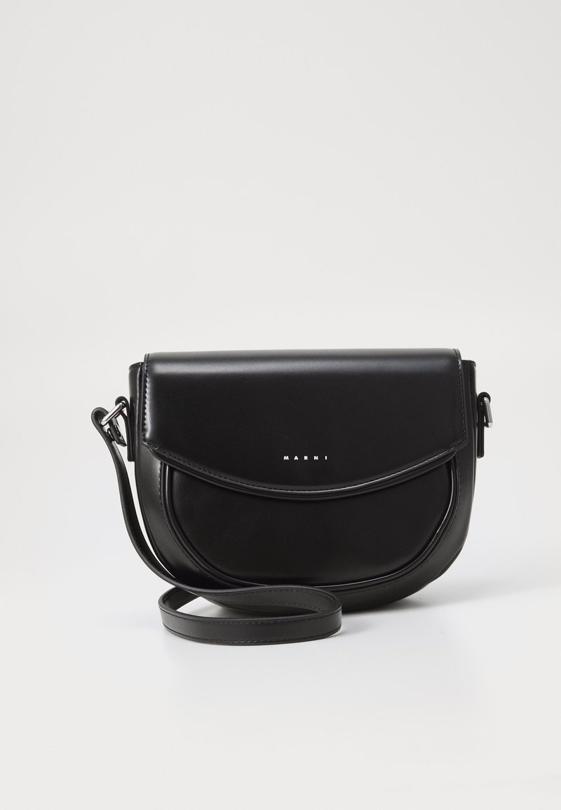 Svart läder crossbody-väska med en rundad klaff, silverlogotyp, justerbar rem och slät textur. Kompakt design med minimala detaljer.