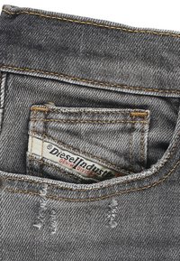 Jeans in denim grigio con una texture strappata, dotati di cuciture arancioni, una piccola tasca frontale e un'etichetta visibile di Diesel Industries.