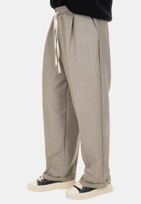 Pantaloni grigi chiari a gamba larga con una finitura texturizzata, dotati di vita elastica con coulisse. Abbinati a sneakers nere e bianche.