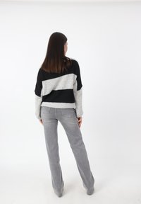 Schwarzer und grauer gestreifter Strickpullover mit lockerer Passform, kombiniert mit grauen Schlaghosen. Der Pullover hat eine weiche Textur und überschnittene Schultern.