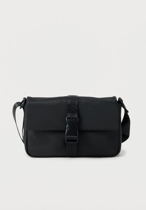 Sac bandoulière rectangulaire noir avec une sangle ajustable et un rabat avant sécurisé par une boucle en plastique centrale et un détail en sangle.