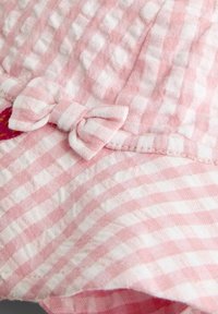 Rozā un baltas ginghama audums ar strukturētu virsmu, ar mazu auduma loku sānos. Dizainam ir krokojums malas malā.