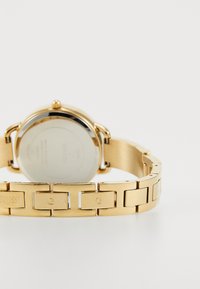 Gold metal watch with a link bracelet. Features a round case, polished and matte finish, and engraved brand detail on the band.