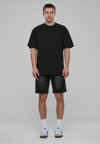 Camiseta negra oversize combinada con pantalones cortos de mezclilla oscuros con un diseño de patchwork. Medias blancas y zapatillas negras completan el atuendo.