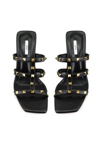 Zwarte haksandalen met vierkante tenen, meerdere decoratieve banden met gouden piramide-nieten, gladde leren textuur en een platte hak.