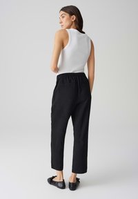 Zwarte, losse broek met een elastische tailleband en zijzakken, gecombineerd met een witte mouwloze top en zwarte platte schoenen.