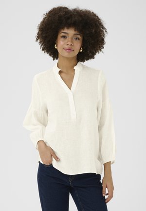 Blusa di lino color crema con colletto a volant, patta con bottoni e maniche svasate. Dettaglio della tasca frontale con design comodo.