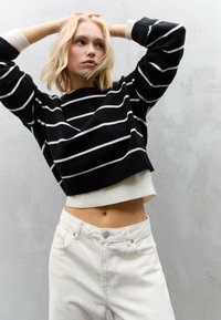 Maglione a strisce bianche e nere con design cropped. Abbinato a jeans bianchi a vita alta con chiusura a bottoni e tasche frontali.