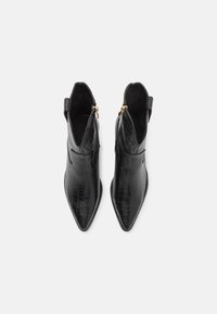 Paire de bottines noires à bout pointu avec texture crocodile et fermetures éclair latérales, vues de dessus sur un fond blanc.