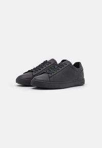 Black leather sneakers with a low-top design, round toe, textured soles, and lace-up closure. Logo embossed on the side.